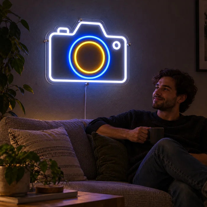 Kamera Neon LED Schild an der Wohnzimmerwand, davor entspannt eine Person auf dem Sofa