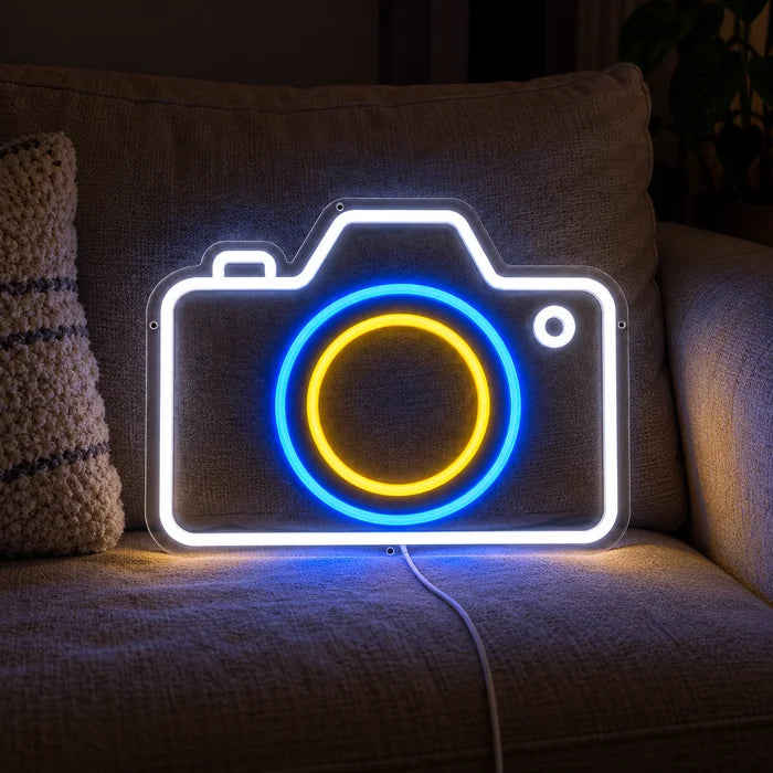 Kamera Neon LED Schild auf einem gemütlichen Sofa zwischen Kissen und Decke