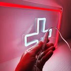 Deko-Leuchtschild in der Form eines weißen Kreuzes, das als medizinisches oder Schweiz Symbol interpretiert werden kann.

