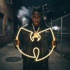 LED-Neon des Wu-Tang Symbols (W) auf einer gelben Ziegelwand montiert, ideal für Hip-Hop Fans.
