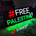 Wanddeko-Leuchtschild mit der Aufschrift FREE PALESTINE und einem roten Hashtag, der sich in der Oberfläche spiegelt.
