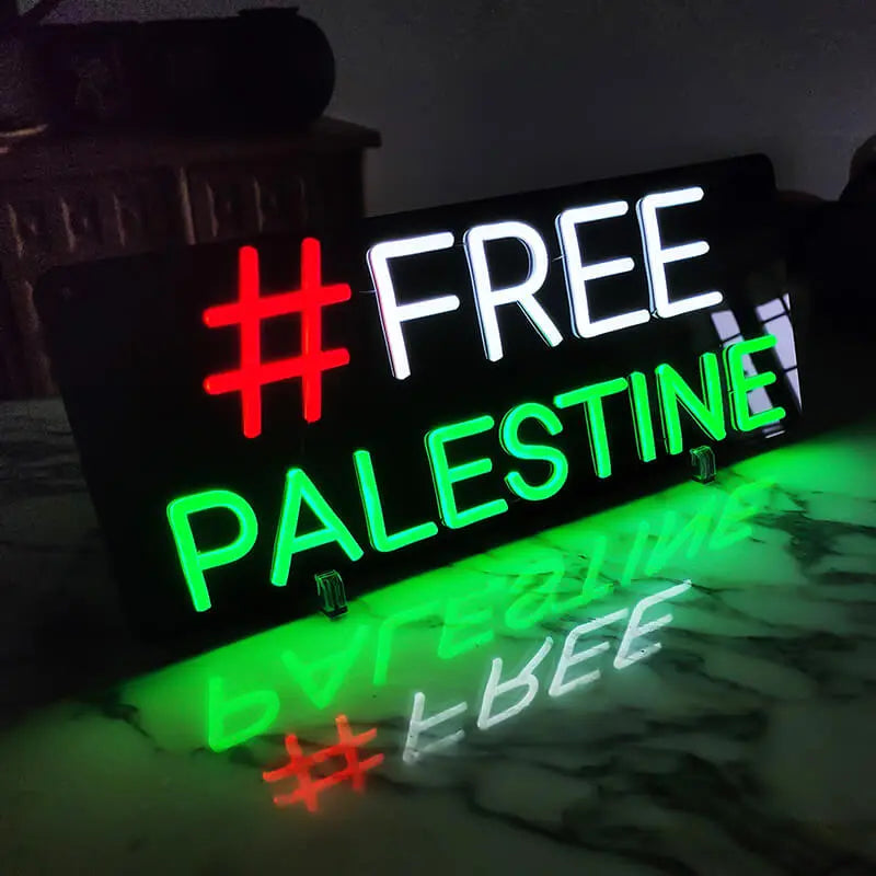 Wanddeko-Leuchtschild mit der Aufschrift FREE PALESTINE und einem roten Hashtag, der sich in der Oberfläche spiegelt.
