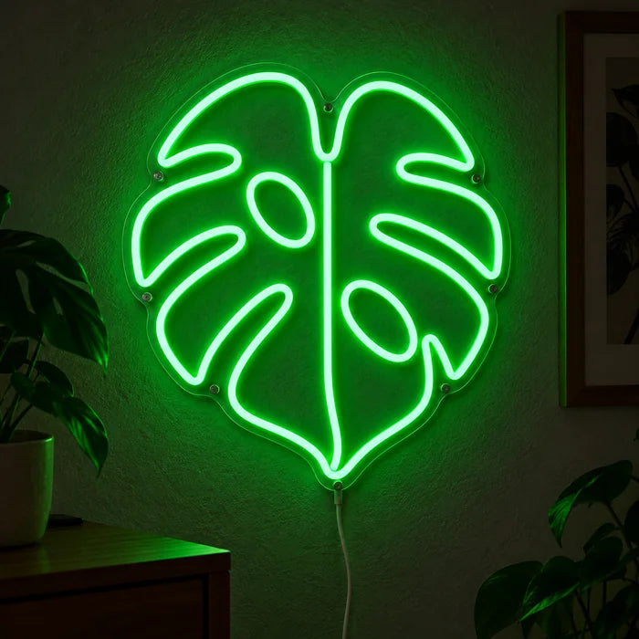 Monstera Neon LED Schild leuchtend an einer dunklen Wand, Nahaufnahme mit Anschlusskabel