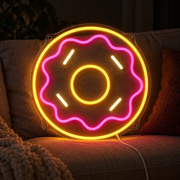Rosa Donut Neon LED Schild auf einem gemütlichen Sofa zwischen Kissen und Decke