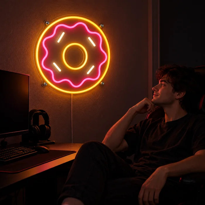 Rosa Donut Neon LED Schild über dem Gaming-Schreibtisch, davor ein Spieler im Gaming-Stuhl