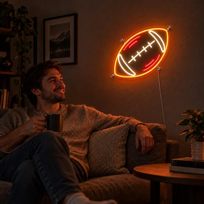 Rugbyball Neon LED Schild an der Wohnzimmerwand, davor entspannt eine Person auf dem Sofa