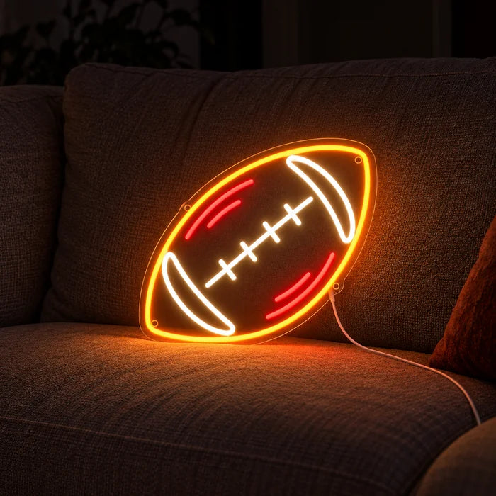 Rugbyball Neon LED Schild auf einem gemütlichen Sofa zwischen Kissen und Decke