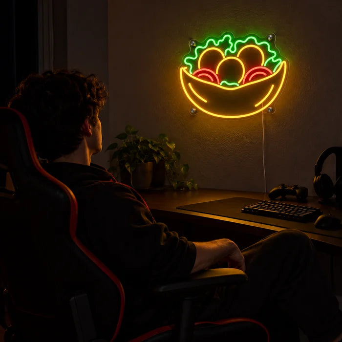 Salatschale Neon LED Schild über dem Gaming-Schreibtisch, davor ein Spieler im Gaming-Stuhl