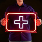 LED-Neon Symbol des Sanitätskreuzes (Erste Hilfe), leuchtend in Weiß und Rot vor einem dunklen Holzhintergrund.
