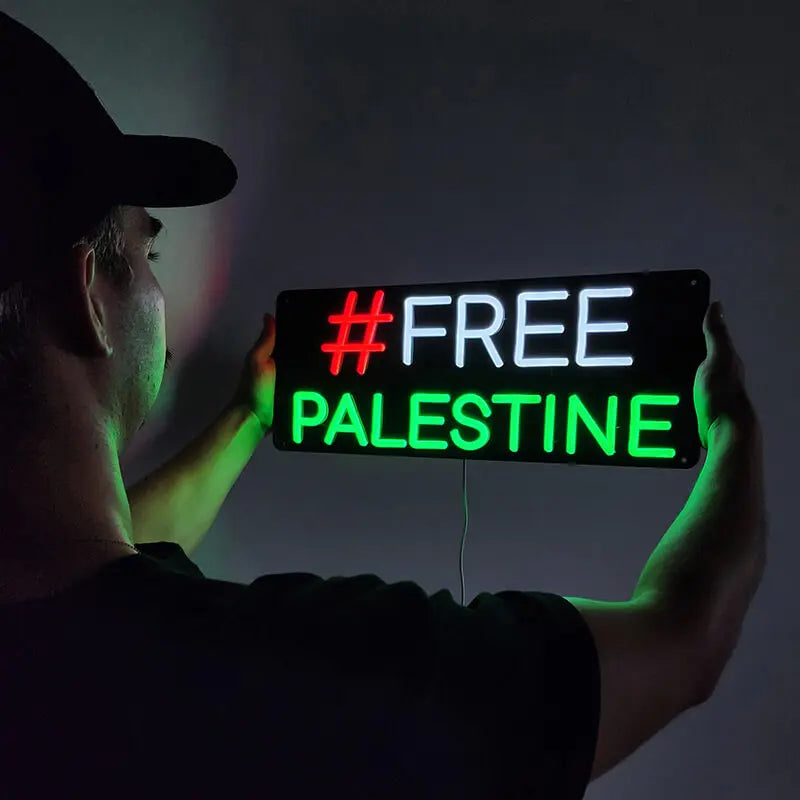 LED-Neon-Leuchtschrift auf schwarzer Platte mit der Aufschrift FREE PALESTINE in den Farben der Flagge.
