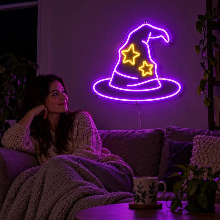 Zauberhut Neon LED Schild an der Wohnzimmerwand, davor entspannt eine Person auf dem Sofa